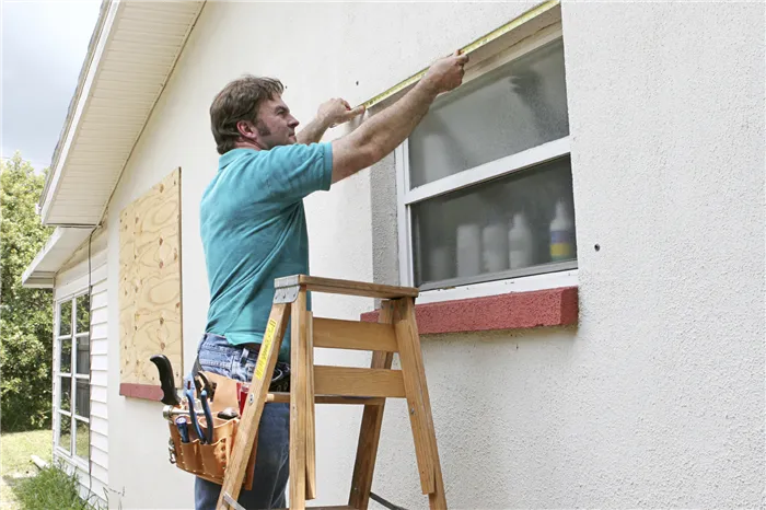 Мужчина измеряет окна для установки ураганных жалюзи или фанеры.